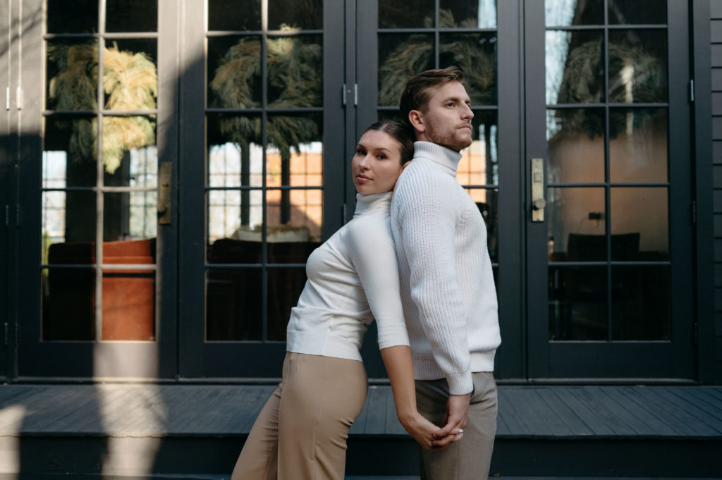 Couple posing back to back in neutral toned outfits 
