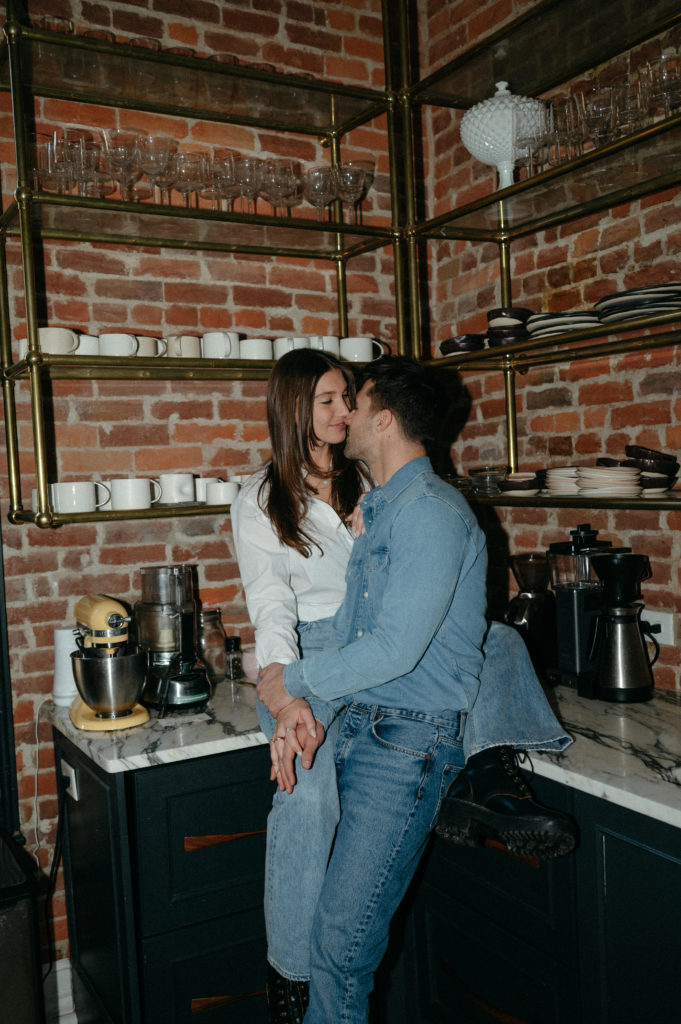 Couple sitting on kitchen counter, kissing, in blue jeans 