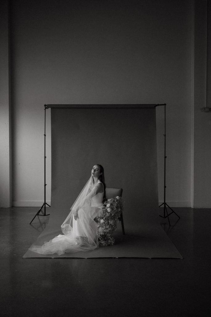 Editorial bride posing in chair in front of a backdrop in black and white 