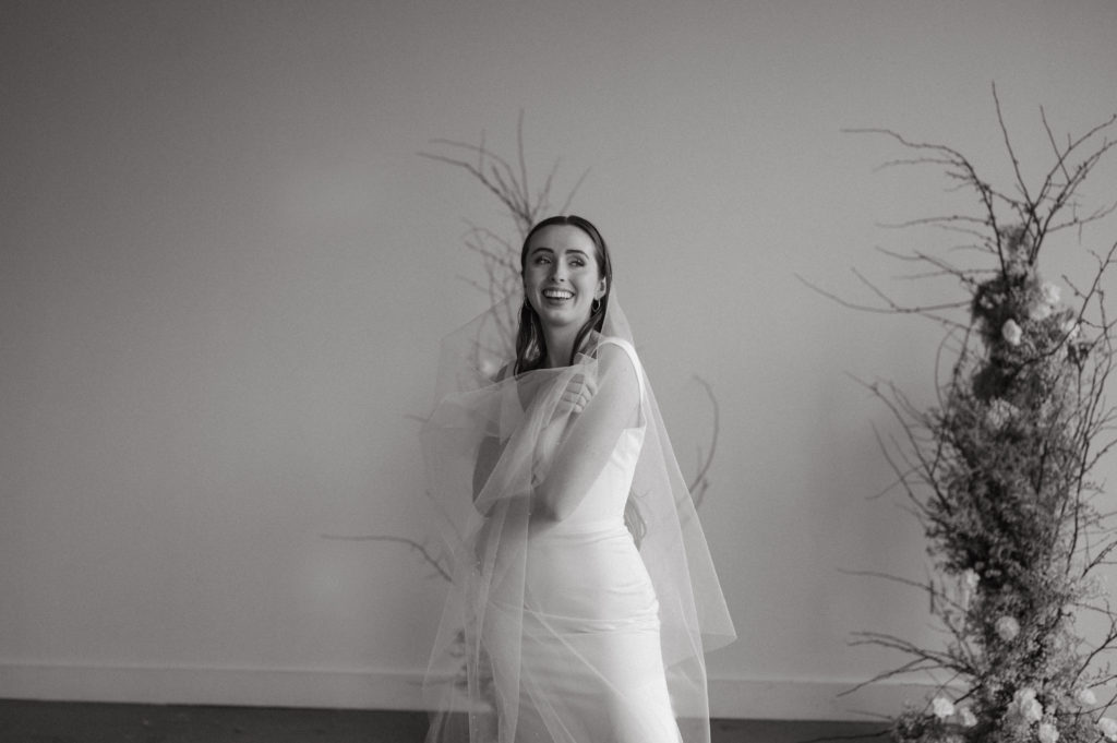 Editorial bride posing with veil in front of floral piece. 