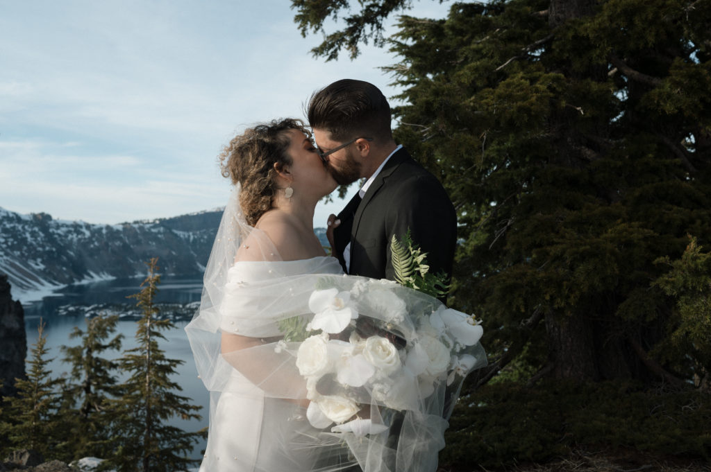 Bride and Groom kissing in front of lake during their Oregon elopement.