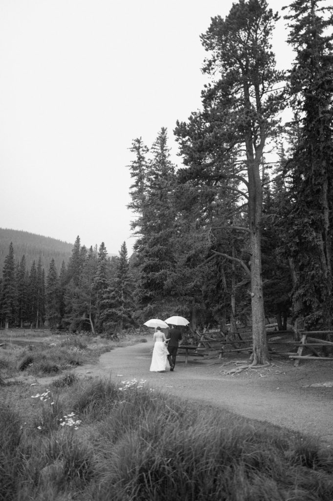 romantic black and white portrait of bride and groom walking along echo lake 