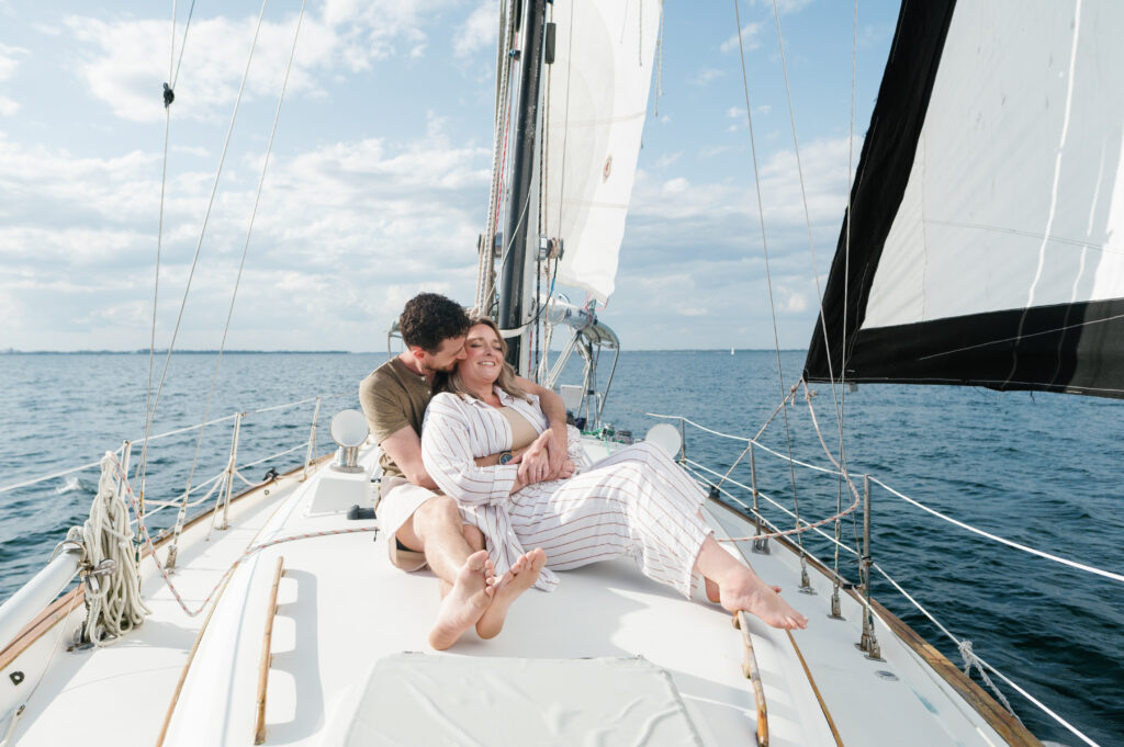 Couple sitting on the front of their sailboat for engagement photos 
