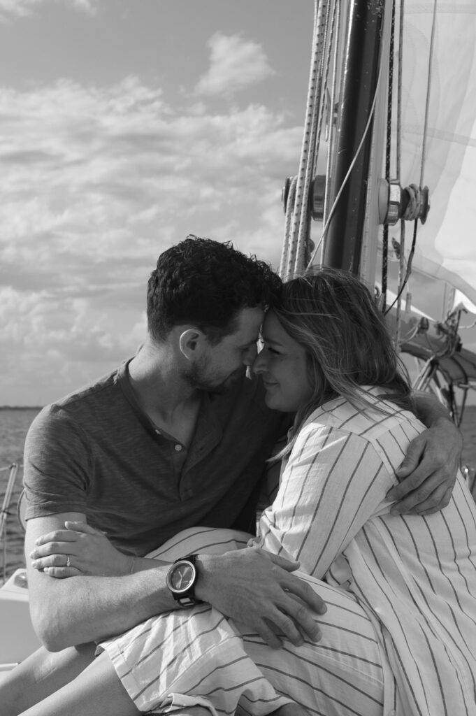 Couple snuggled together on the front of their sailboat for engagement photos 