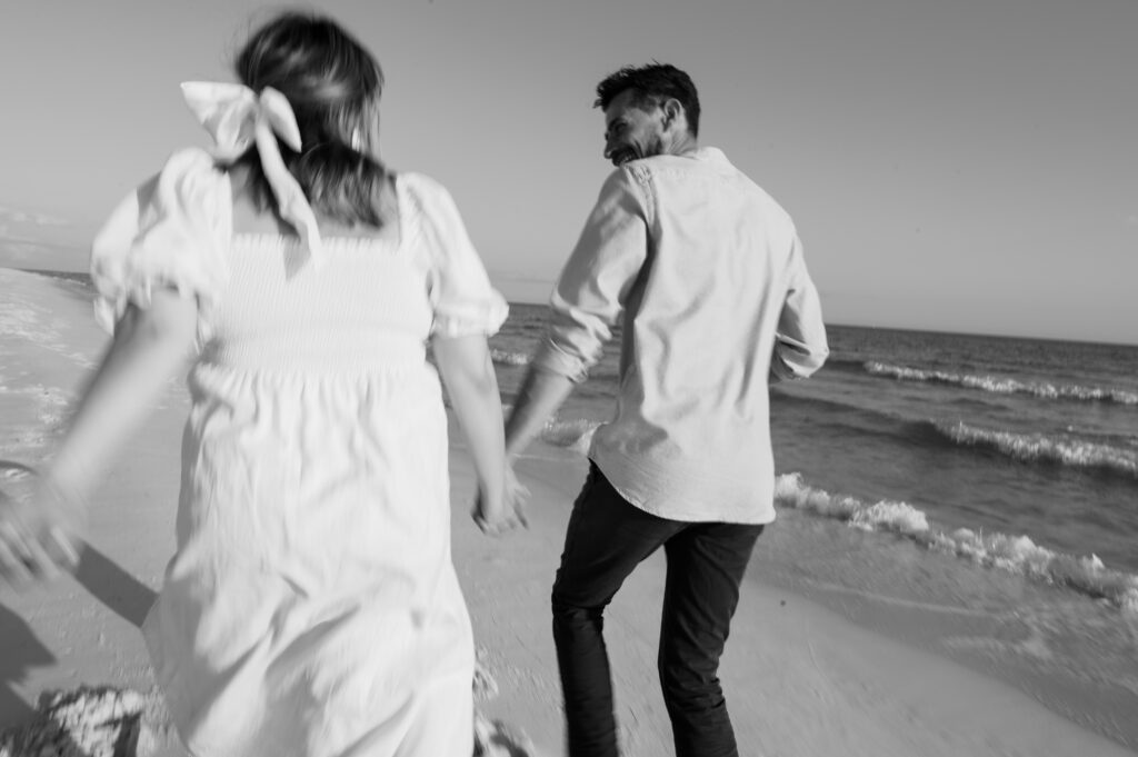 Black and white photo of a couple running along the beach 