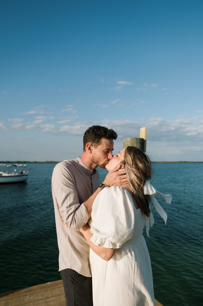 Couple kissing on dock in Florida with their sailboat in the bay behind them