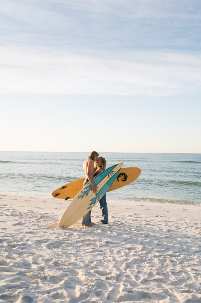 Couple kissing near the ocean with surfboards at sunrise 