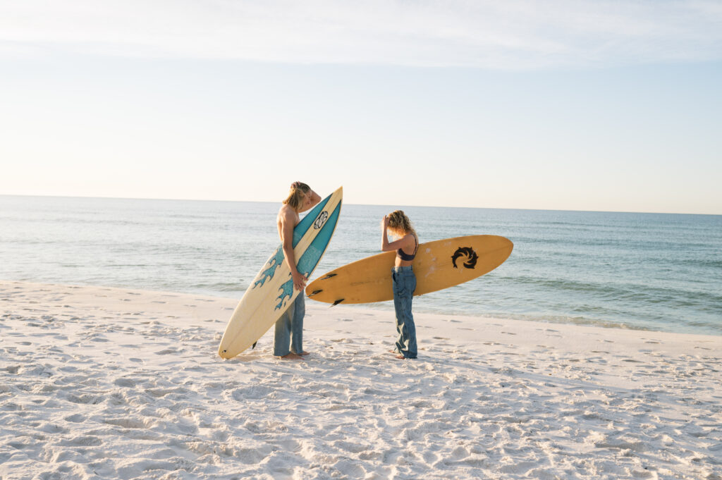 Couple walking towards the ocean with surfboards at sunrise 
