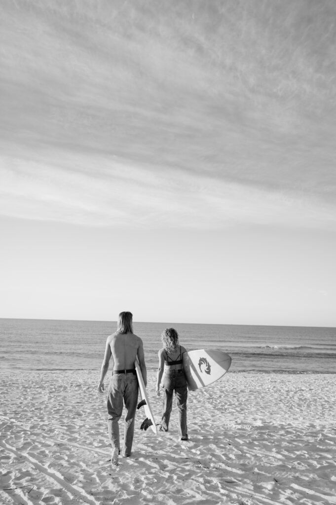 Couple walking towards the ocean with surfboards at sunrise 