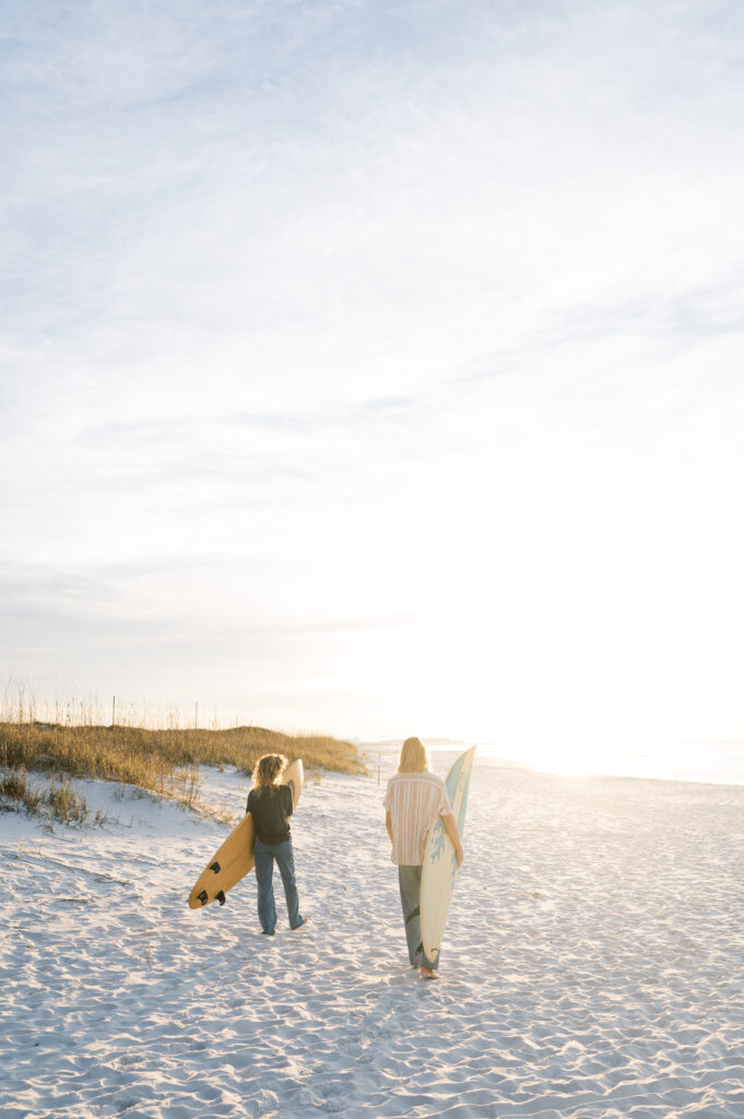 Couple walking on the beach at sunrise with their surfboards 