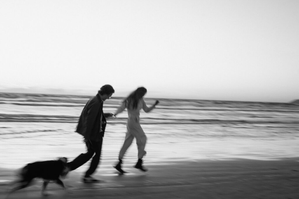 black and white image of couple running on the beach in california 