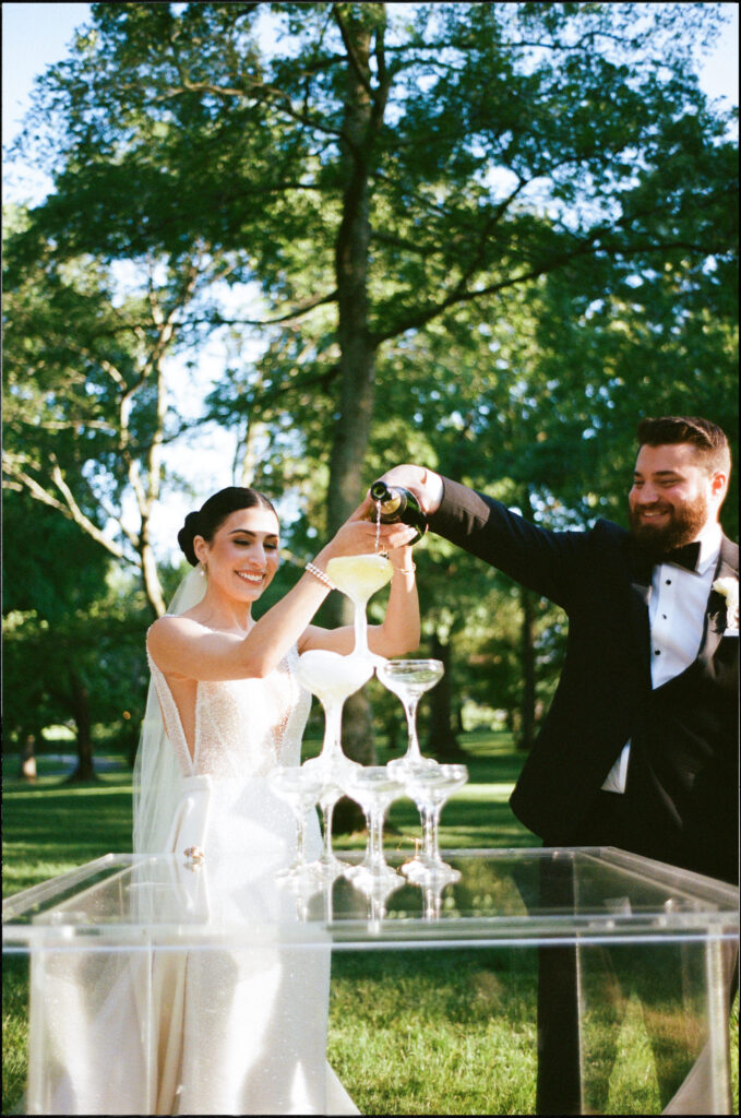 Bride and Groom doing a Champagne tower photographed on film for their wedding ceremony in the front lawn  at The Estate at Cherokee Dock in Nashville, Tennessee