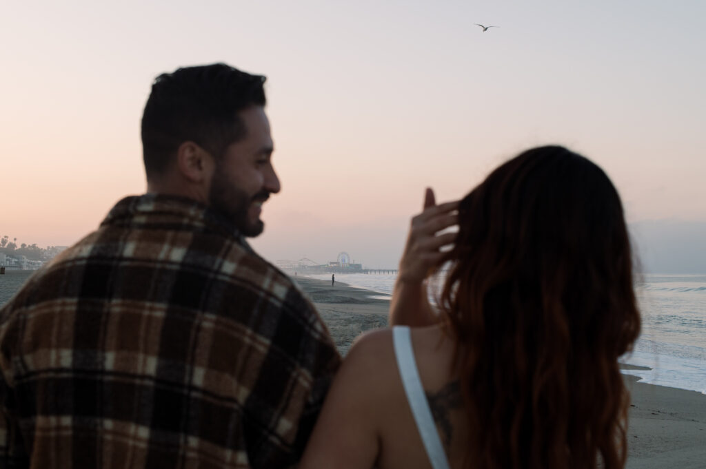 A couple walking on the beach in Santa Monica with The Santa Monica Pier behind them 