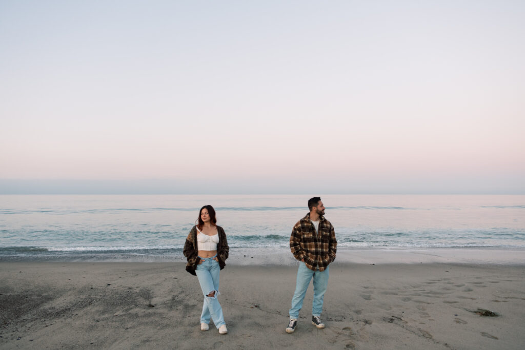 Couple standing on the beach in Santa Monica with pink and blue sunrise colors behind them 