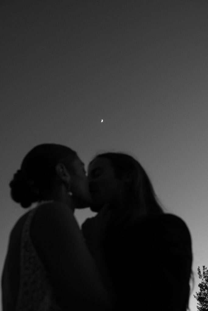 Couple kissing in the foreground ,out of focus, with the moon in focus behind them 