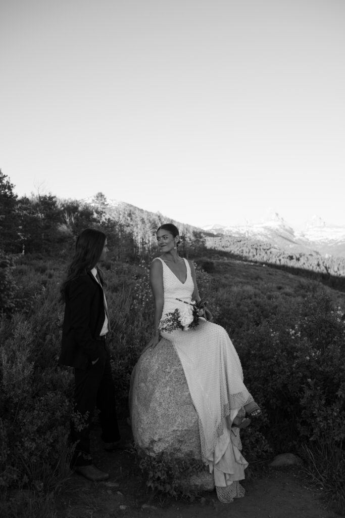 Bride sitting on a rock, looking at groom in front of the Grand Teton Mountain Range 