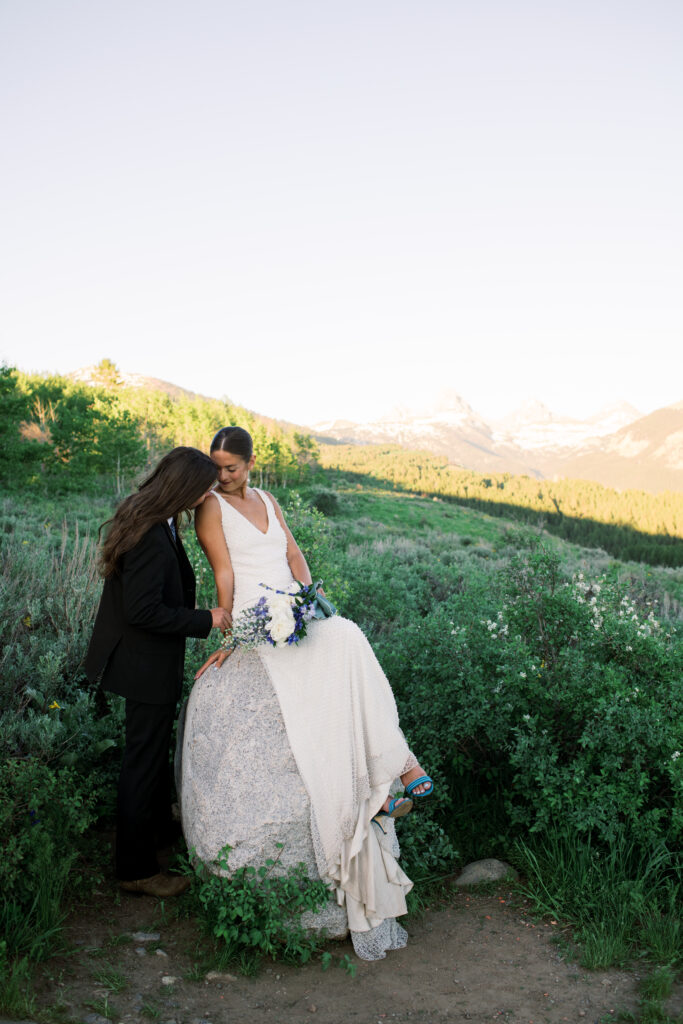 Bride sitting on a rock, looking at groom in front of the Grand Teton Mountain Range 