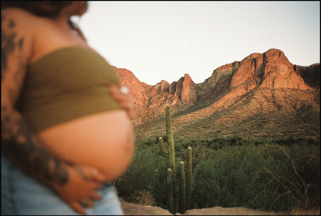 35mm film photo of the Arizona mountains in the distance in focus and a pregnant belly in the foreground