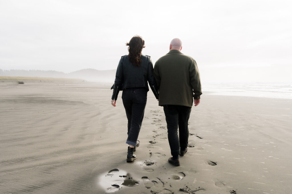 A couple walking away from the camera during their PNW Engagement session on the coast in Seaview, Washington