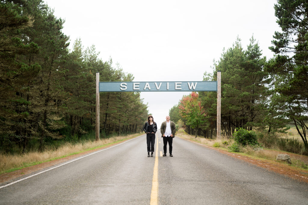 A couple posing under the "Seaview" sign during their PNW Engagement session on the coast in Seaview, Washington