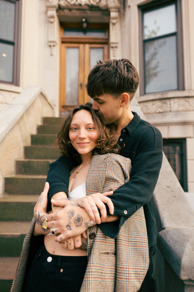 Couple snuggling on the front stoop of a Brooklyn Brownstone during their Engagement session