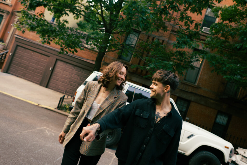 Couple walking toward the camera while holding hands with a vintage Land Cruiser behind them in Brooklyn, New York during their engagement session