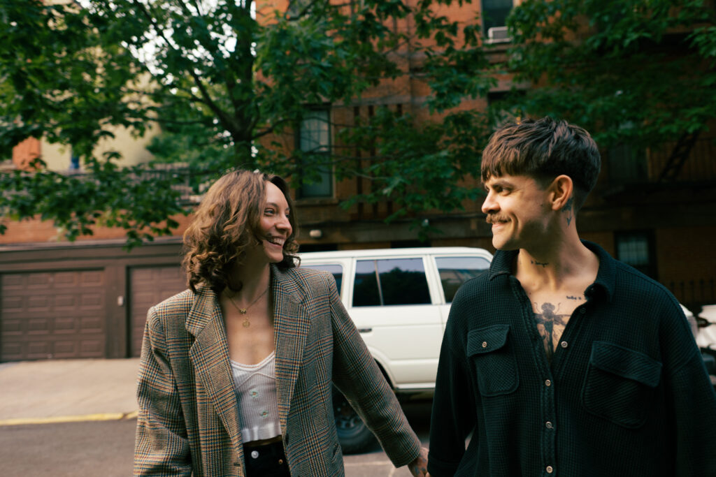 Couple walking toward the camera while holding hands with a vintage Land Cruiser behind them in Brooklyn, New York during their engagement session