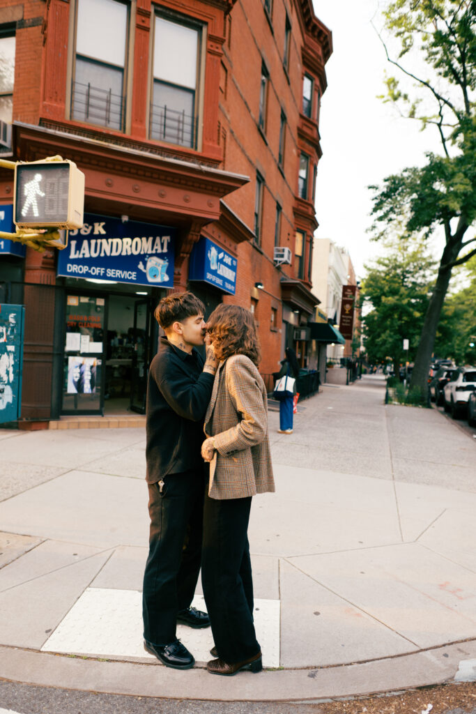 Couple kissing with the setting sun behind them on the street in Brooklyn during their engagement session