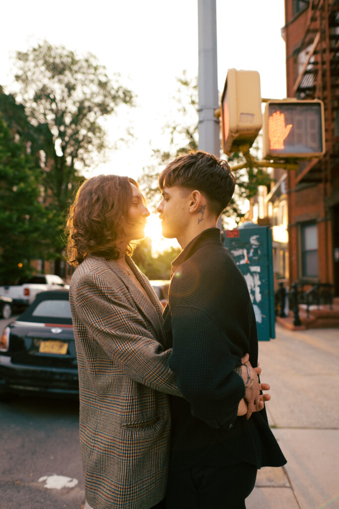 Couple kissing with the setting sun behind them on the street in Brooklyn during their engagement session