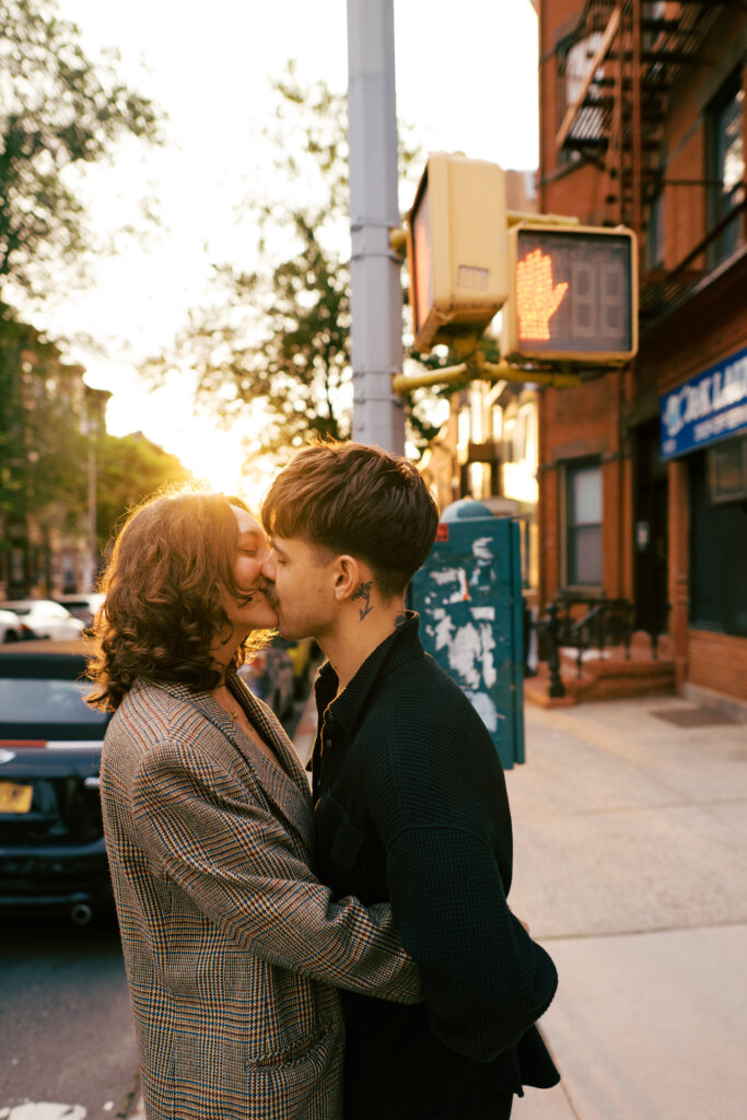 Couple kissing with the setting sun behind them on the street in Brooklyn during their engagement session
