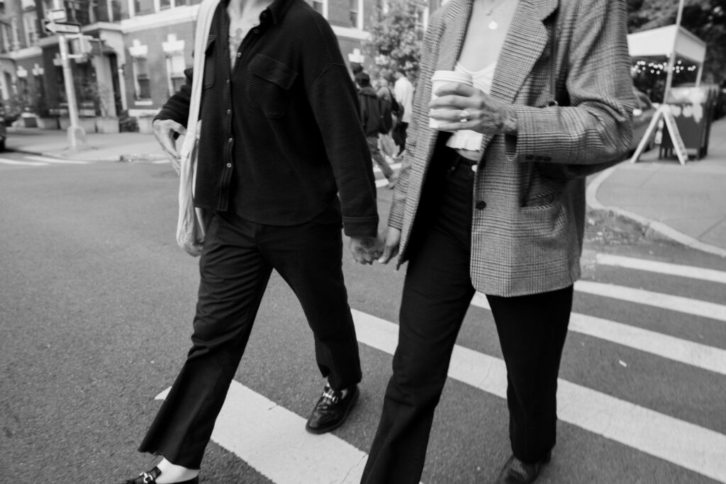Black and white image cropped in at the waist of a couple walking across the street in Brooklyn during their engagement session