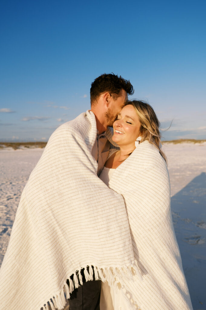 A couple snuggled in a blanket on the coast in Wilmington, North Carolina for their engagement sesion