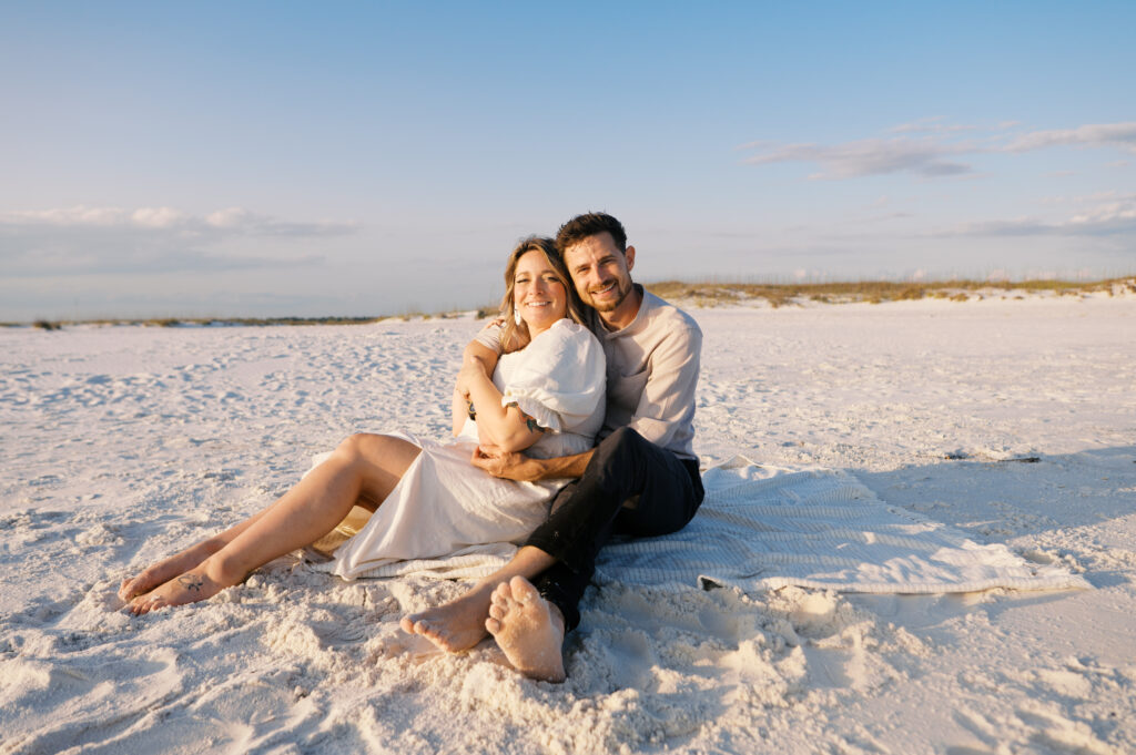 A couple snuggled in a blanket on the coast in Wilmington, North Carolina for their engagement sesion