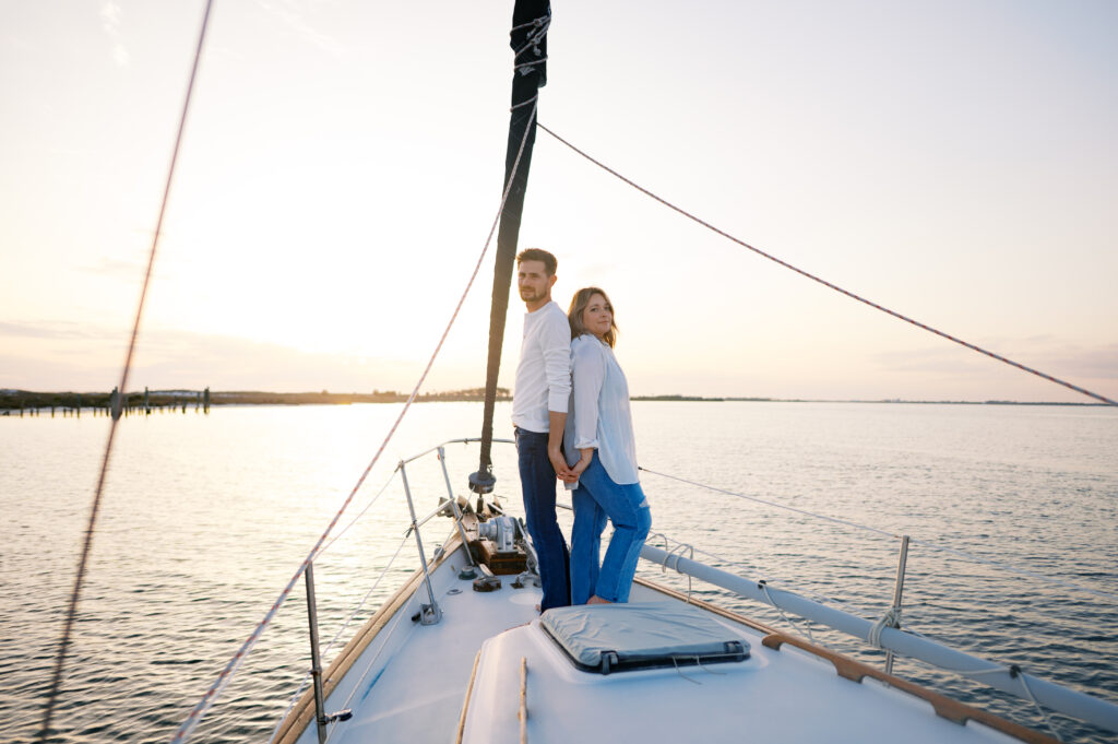 A couple posing on their sailboat for their engagement photos off the coast in Wilmington, North Carolina