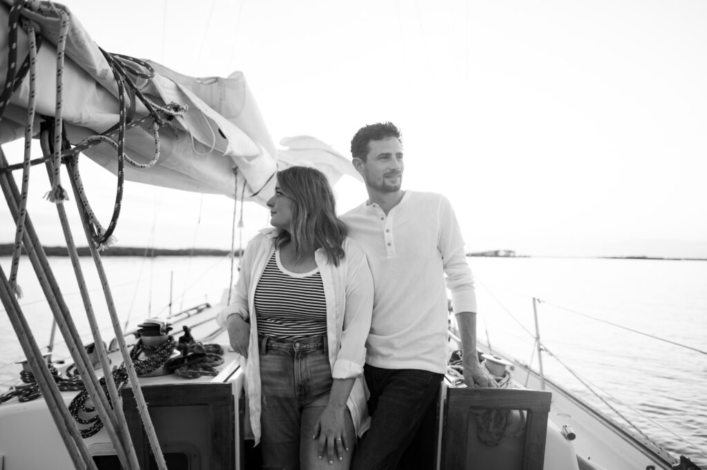 A couple posing on their sailboat for their engagement photos off the coast in Wilmington, North Carolina