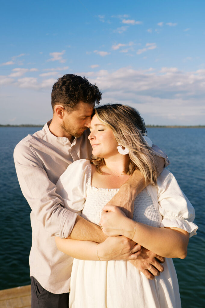 Photo of a couple snuggled with each other in Wilmington, North Carolina at their engagement session on a dock on the coast