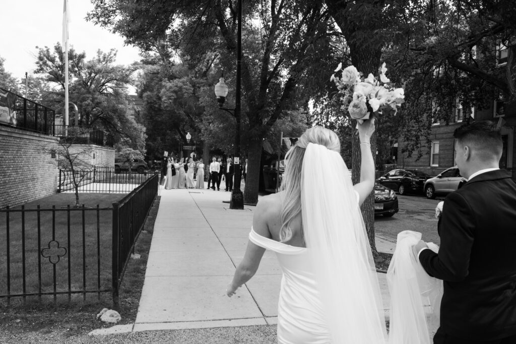 A black and white image of a couple walking back to their wedding party cheering 