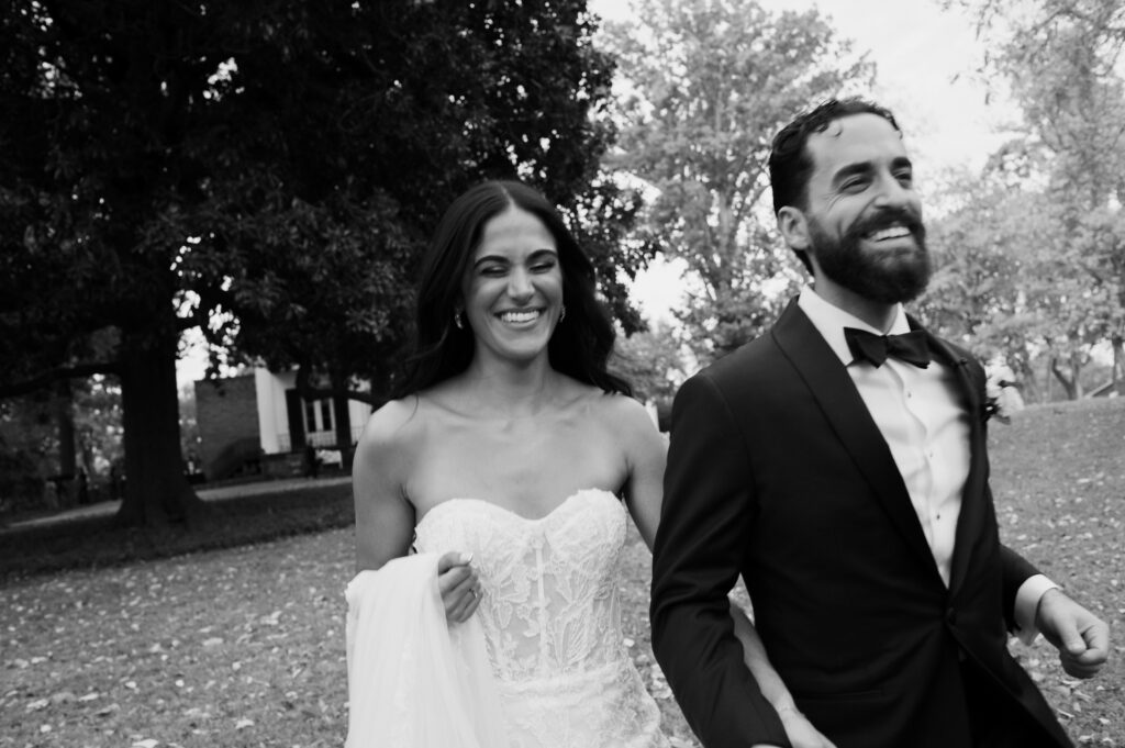 Black and white image of a couple running in the front yard of their venue on their wedding day captured by Wilmington Wedding Photographer Bri Nicole Photo Co.